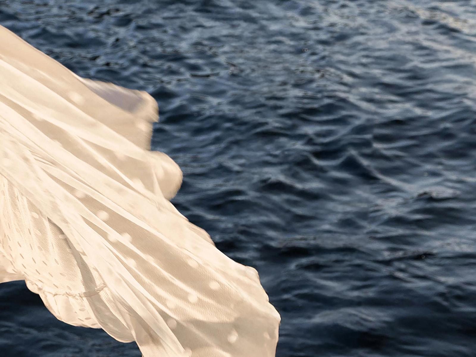 A wedding dress catching the wind over the water