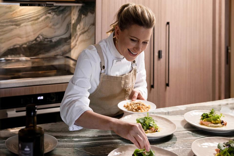 A chef smiling while plating dishes at a marble kitchen counter