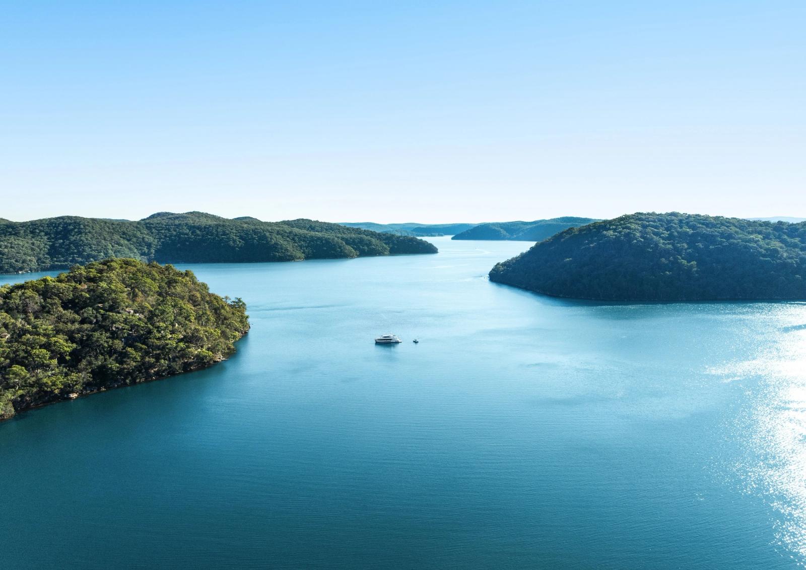 A single yacht at anchor in a vast blue-water cove, seen from the air