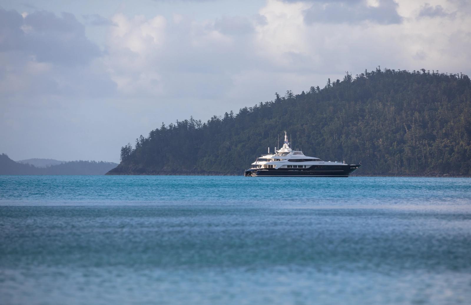A superyacht at anchor under a forested island headland