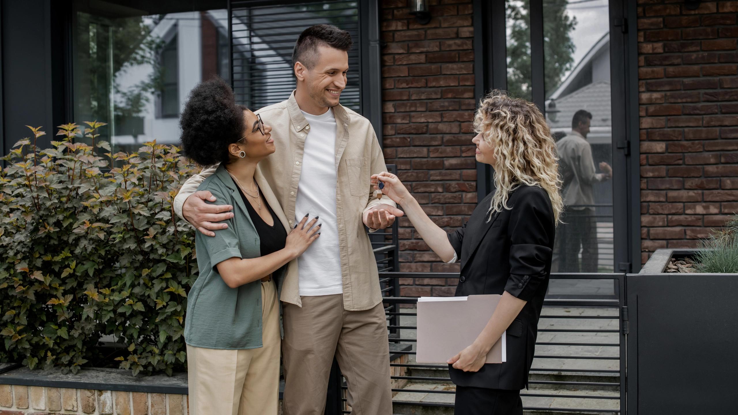 Couple receiving house keys from a real estate agent outside a modern home.