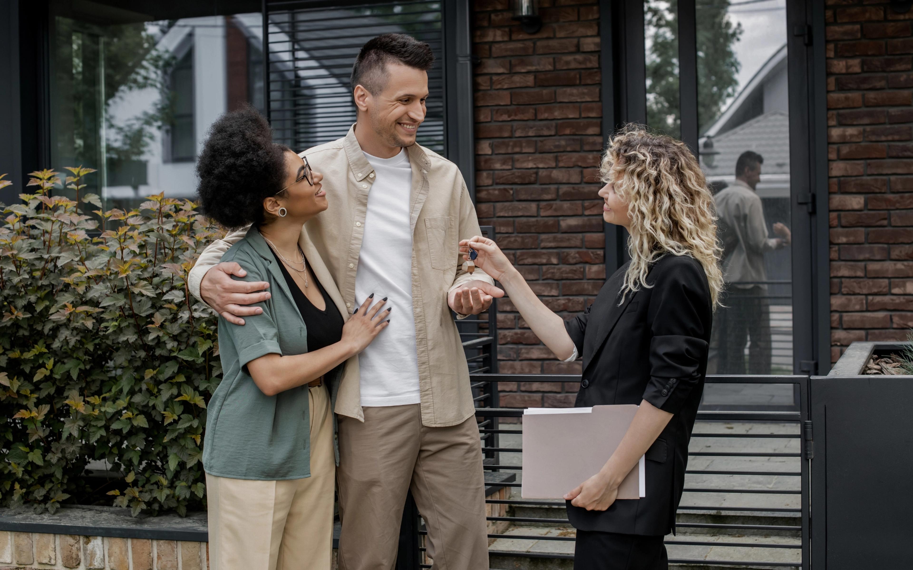 Couple receiving house keys from a real estate agent outside a modern home.