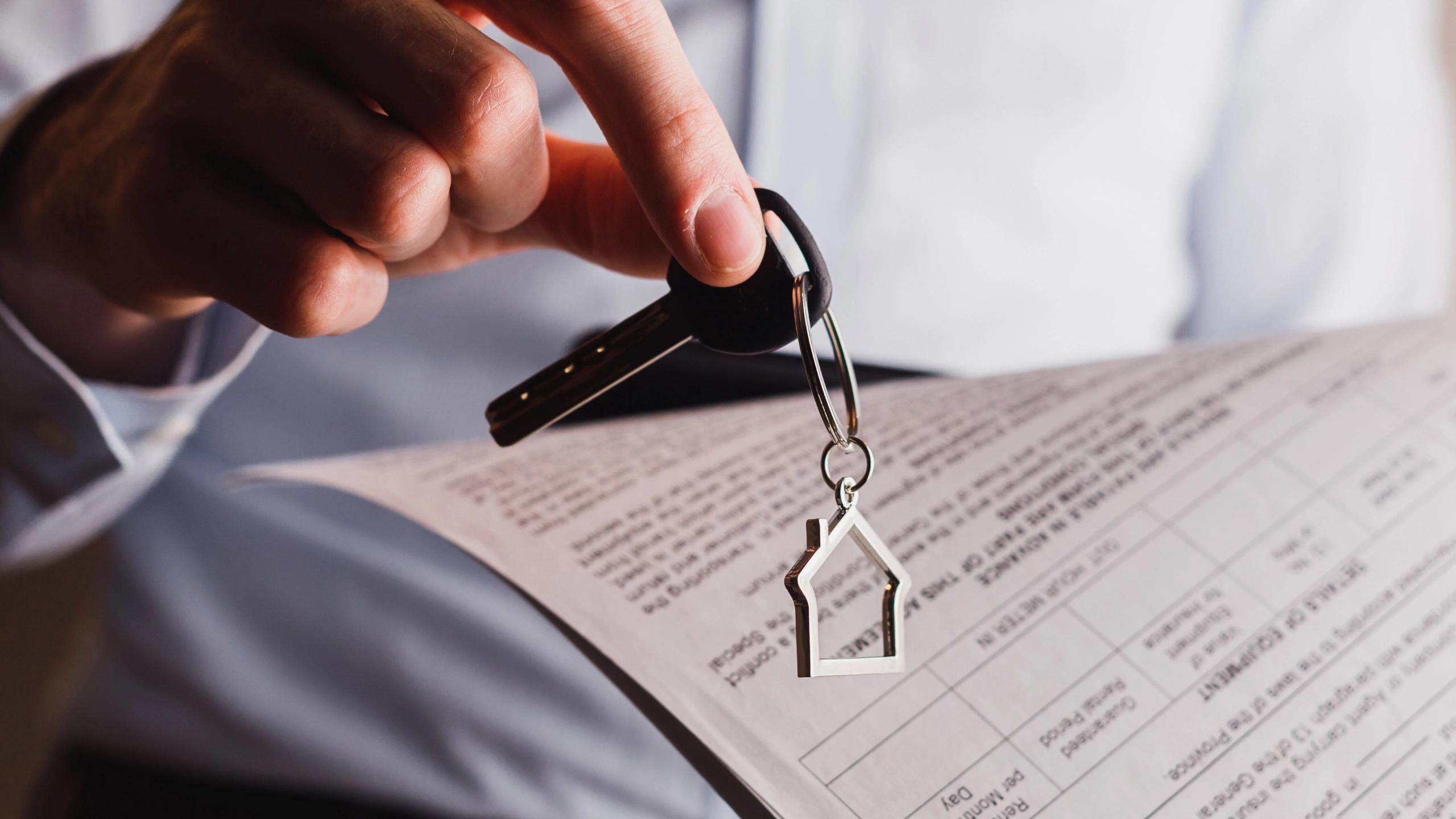 Hand holding a house key over a property contract document.