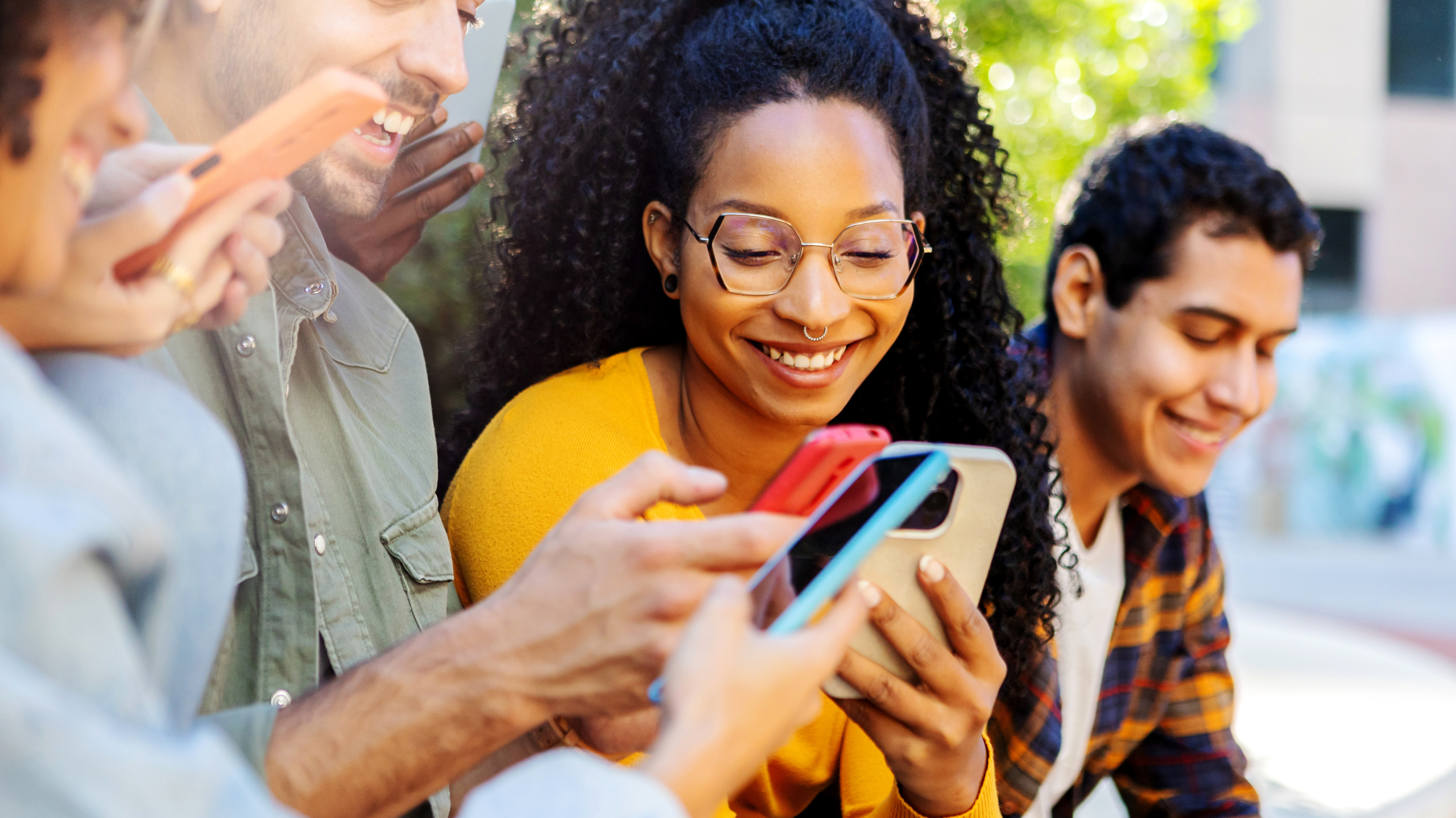 A group of people smiling while looking at smartphones together, representing social media engagement and shared digital interaction.