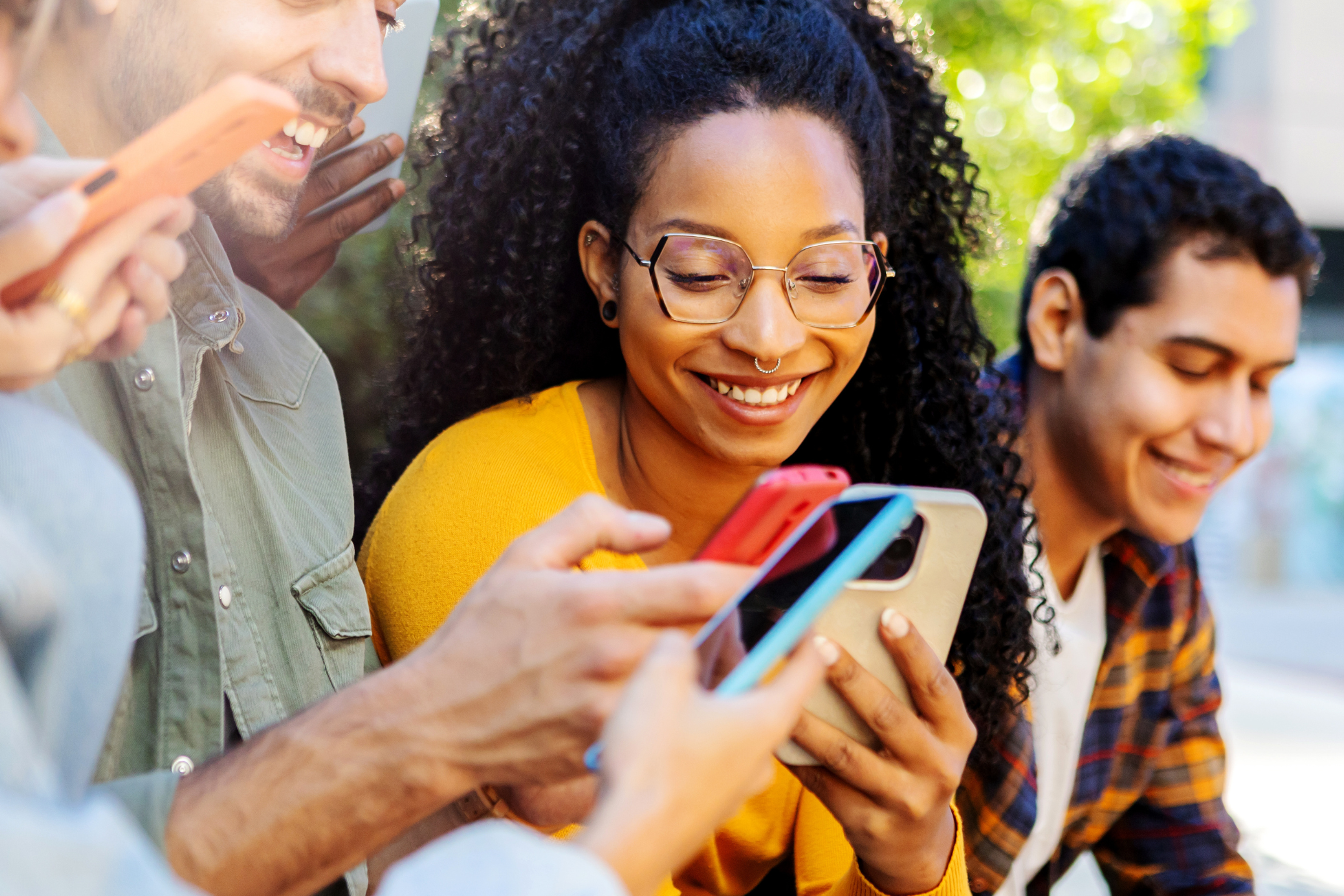 A group of people smiling while looking at smartphones together, representing social media engagement and shared digital interaction.