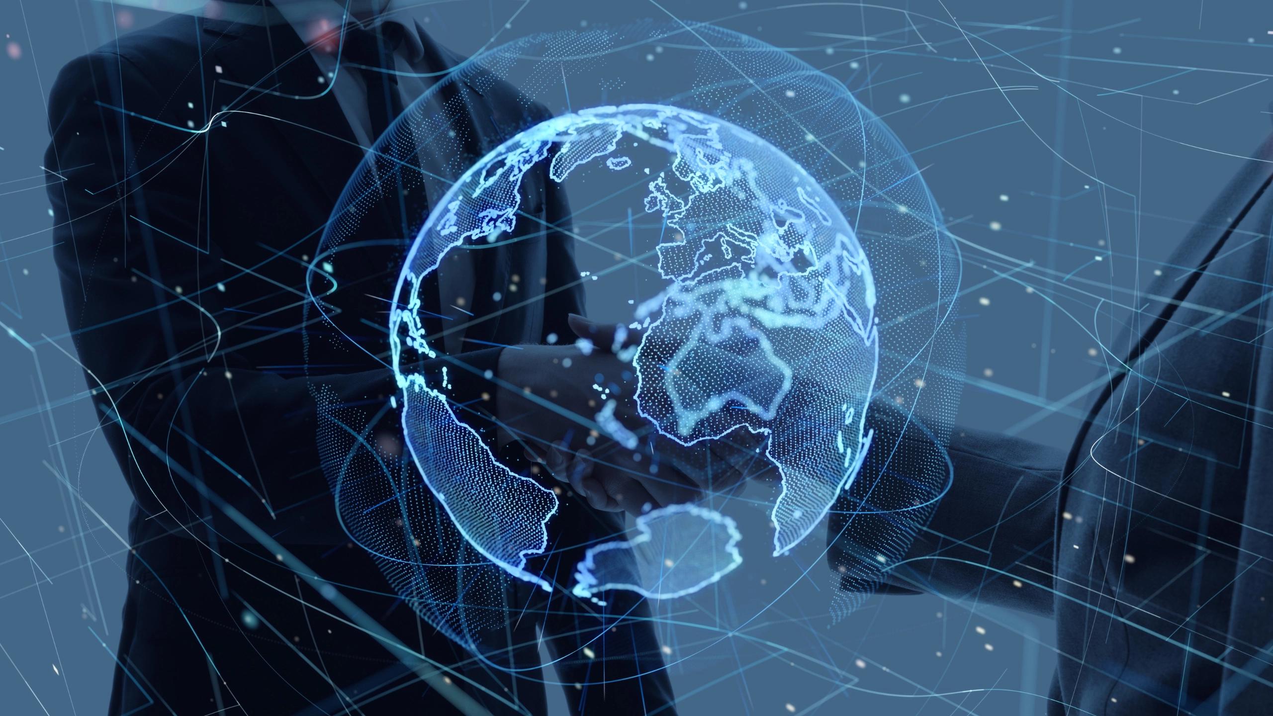 Two suited professionals shake hands enclosing a glowing blue holographic Earth globe