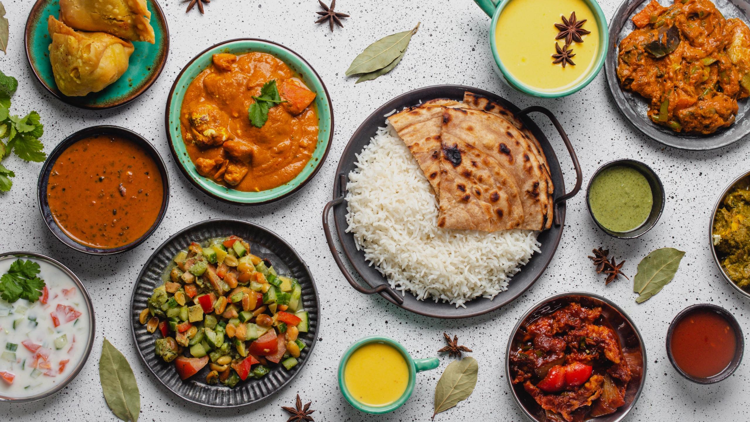Assorted Indian dishes with rice, curry, naan and sides arranged on a table.
