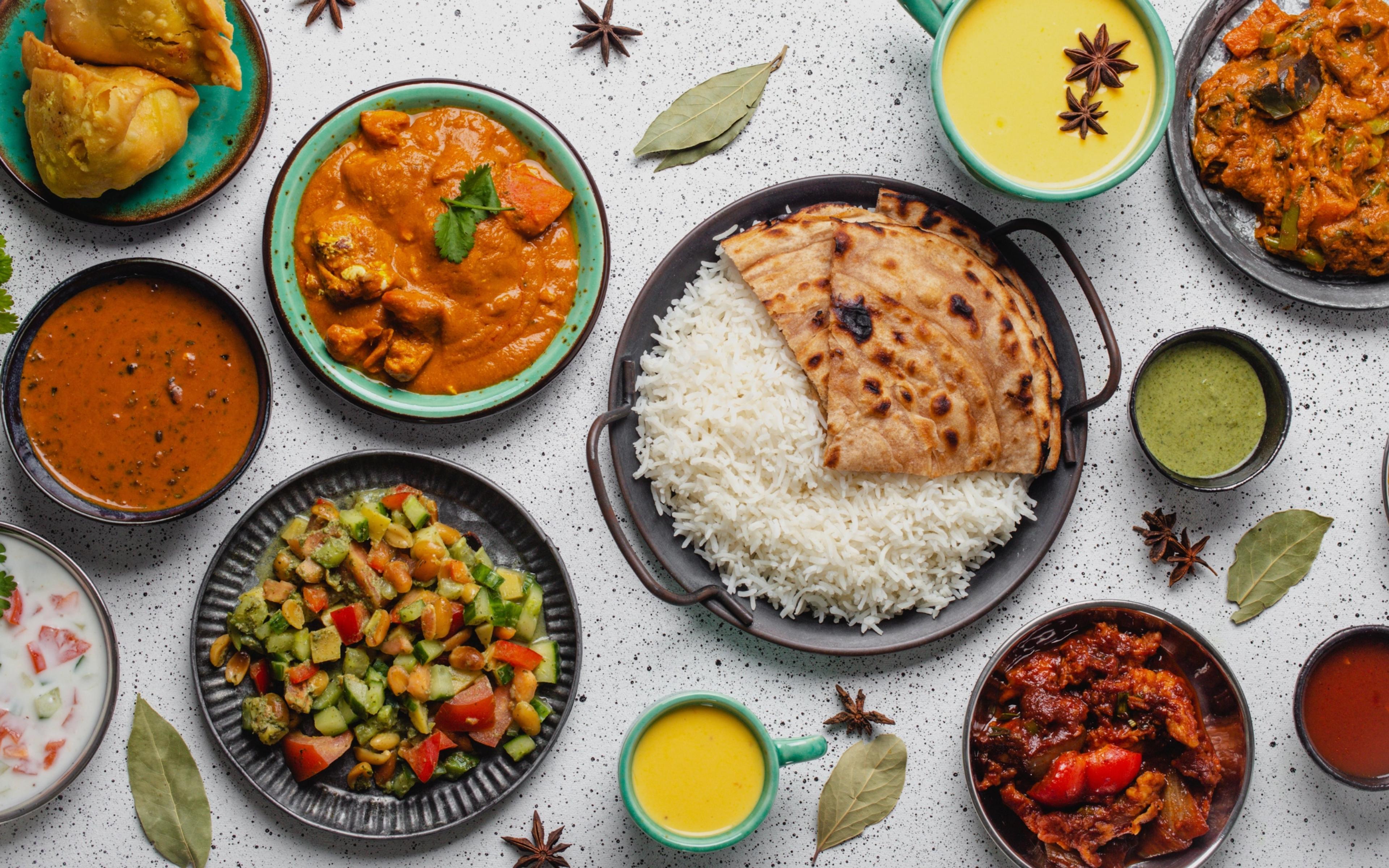 Assorted Indian dishes with rice, curry, naan and sides arranged on a table.