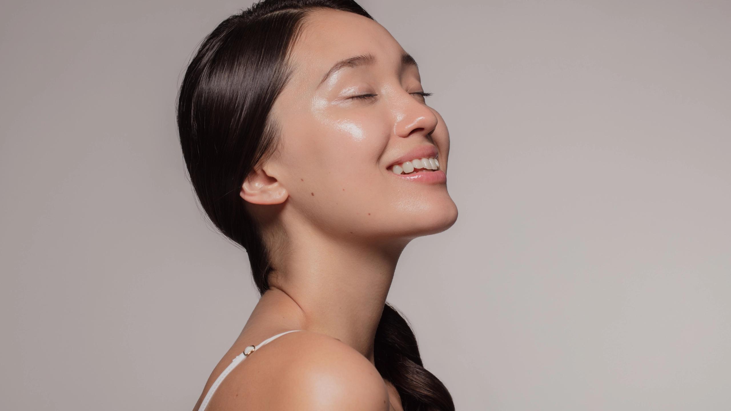 Woman smiling in profile with clear glowing skin against a neutral background.