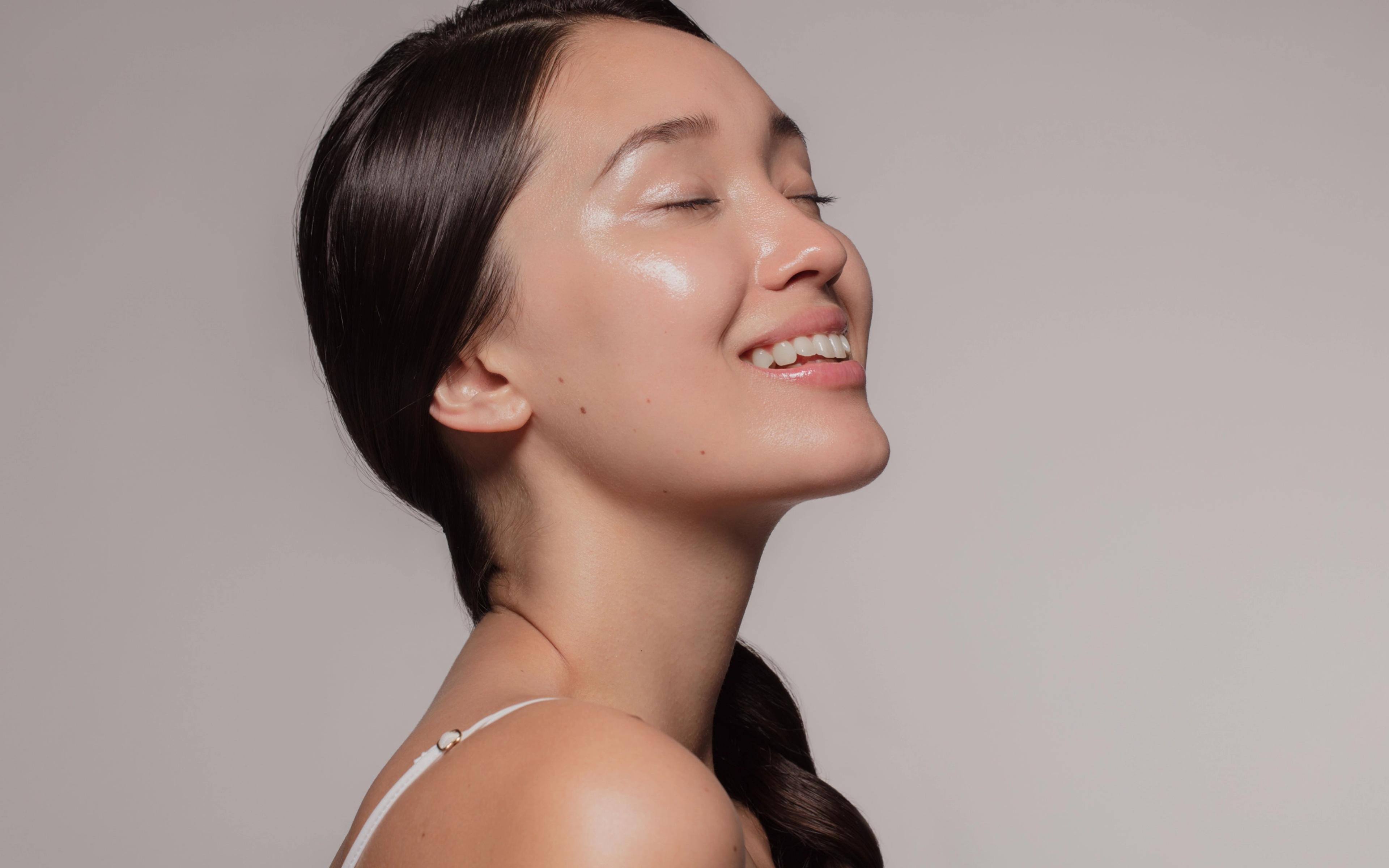 Woman smiling in profile with clear glowing skin against a neutral background.