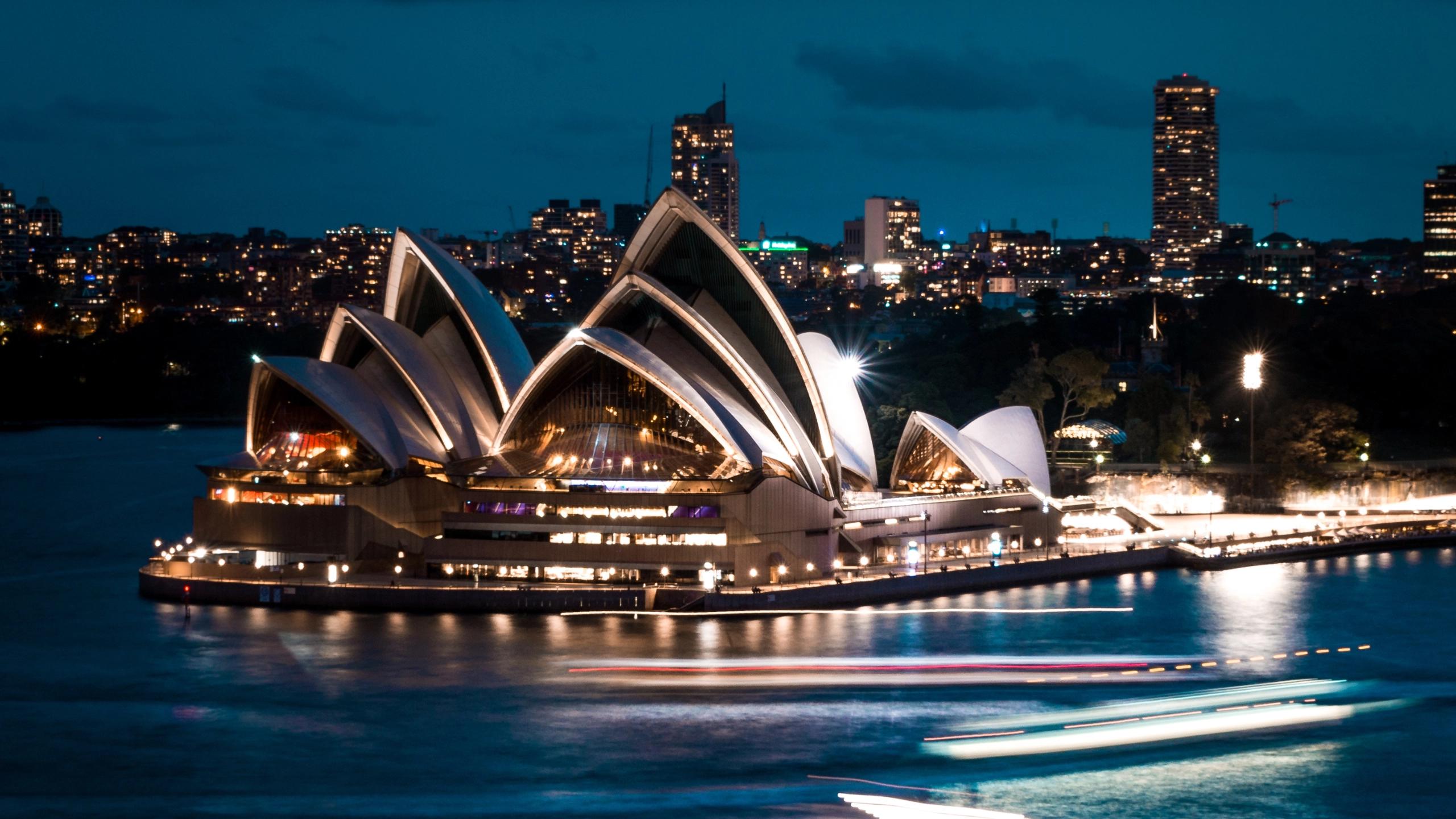 Sydney Opera House illuminated at night beside harbor with light trails and city skyline