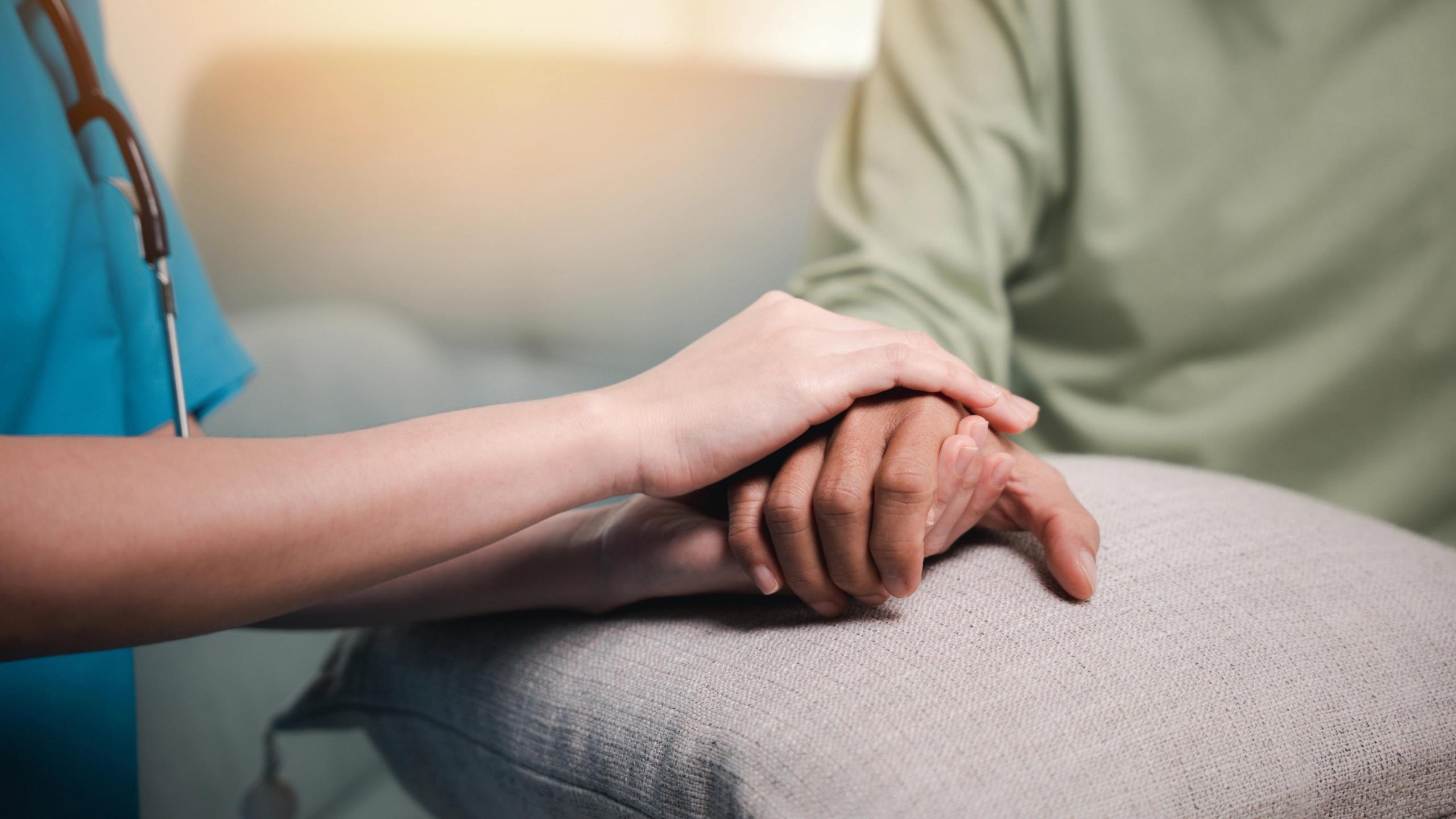 Care worker gently holding a patient’s hand in support.