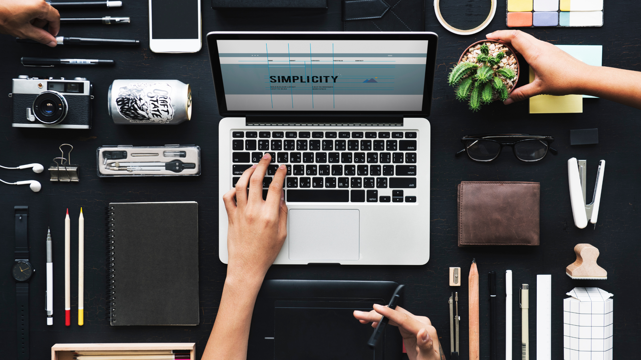 Designer working on a laptop with the word “Simplicity” on screen, surrounded by creative tools and branding materials arranged neatly on a desk.