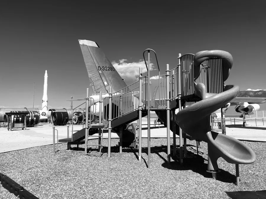 in black and white, a children's playground with nuclear bomber and missile in the background 