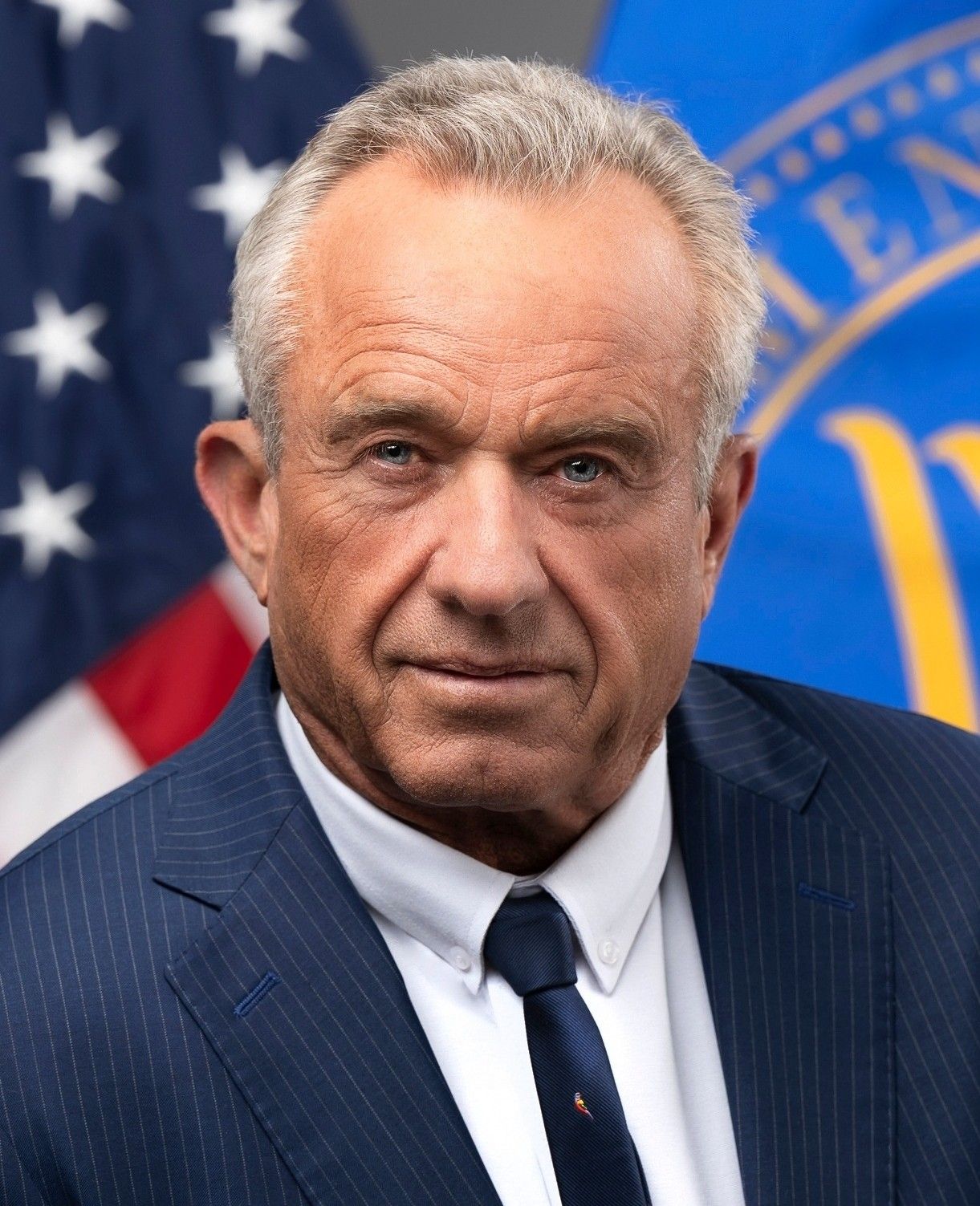 Robert F. Kennedy Jr. in a navy pinstripe suit in front of an American flag