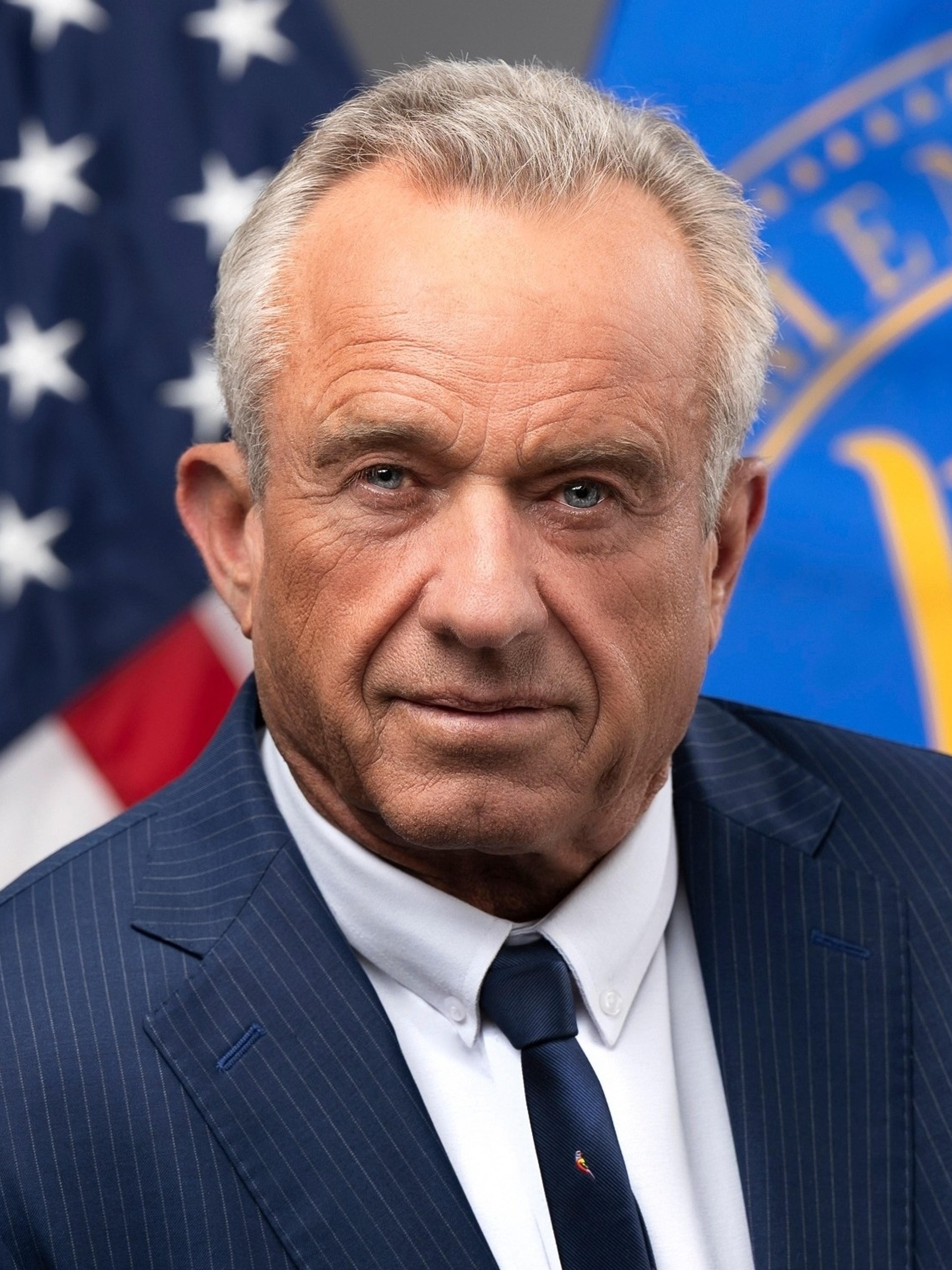 Robert F. Kennedy Jr. in a navy pinstripe suit in front of an American flag