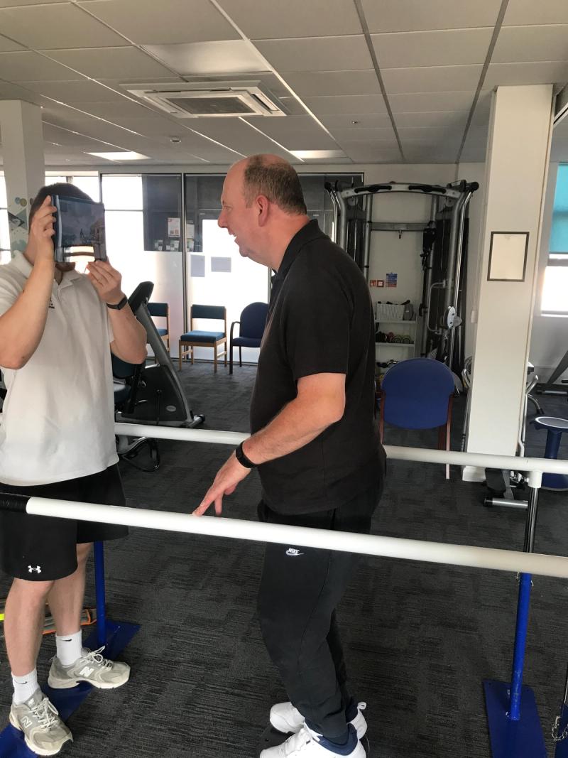 A physiotherapist guiding a client through balance work at the parallel bars