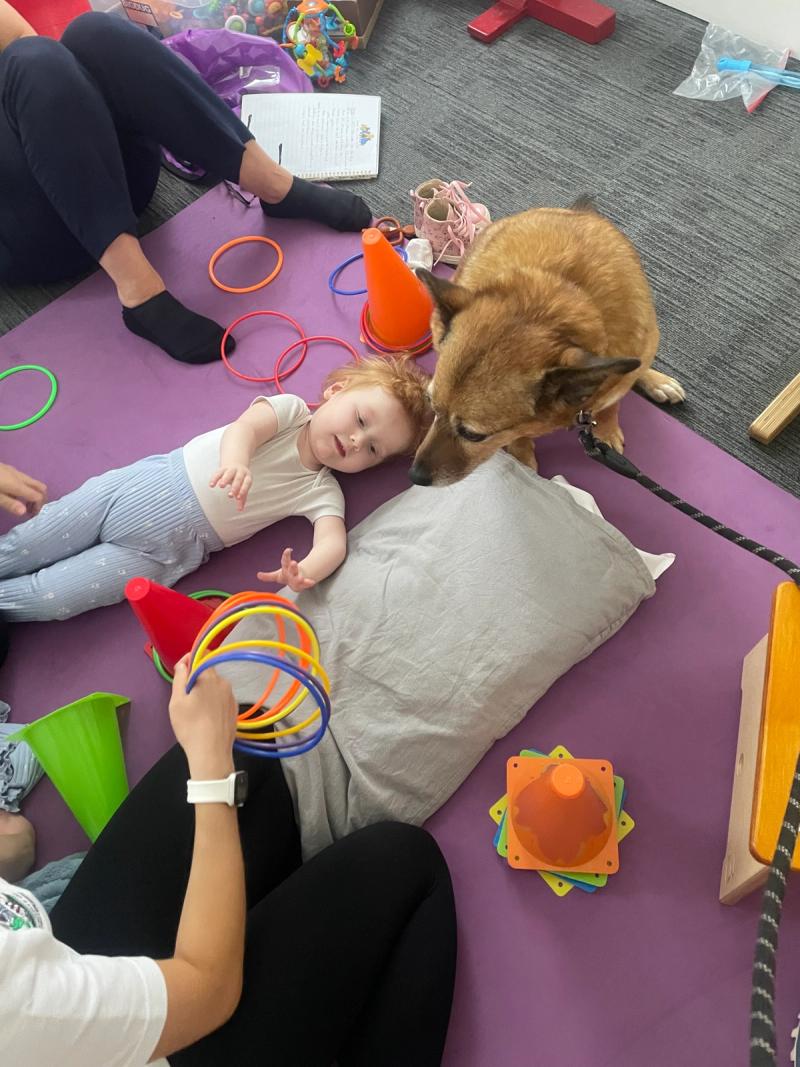A child lying on the therapy mats during a session, with a dog settled alongside