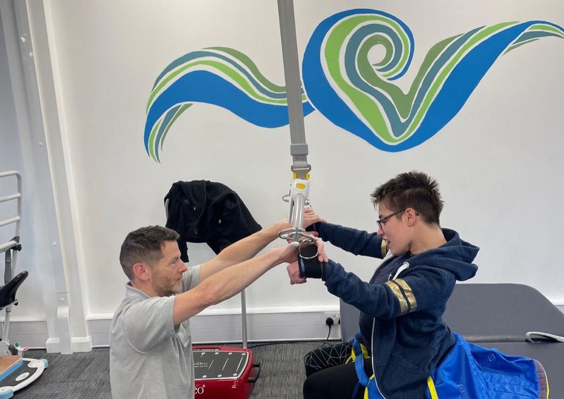 Inside the clinic: a physiotherapist and a young client using the overhead hoist in the rehabilitation gym