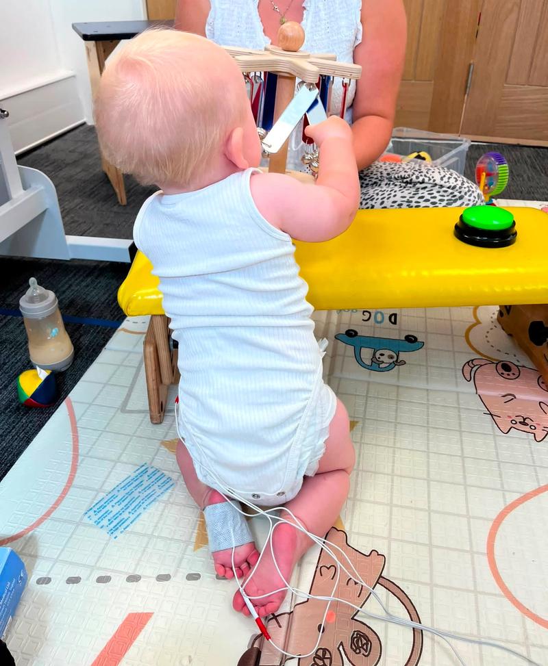 A baby sitting to play at a bench with stimulation electrodes attached