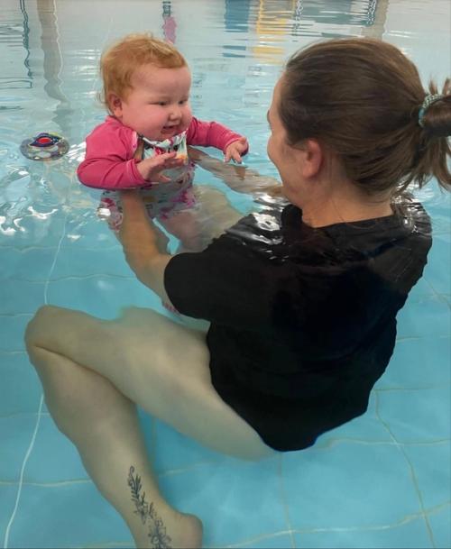 A physiotherapist supporting a smiling baby in the warm water of the hydrotherapy pool