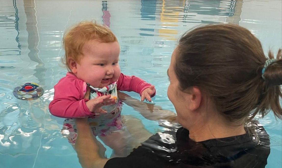 A physiotherapist supporting a smiling baby in the warm water of the hydrotherapy pool