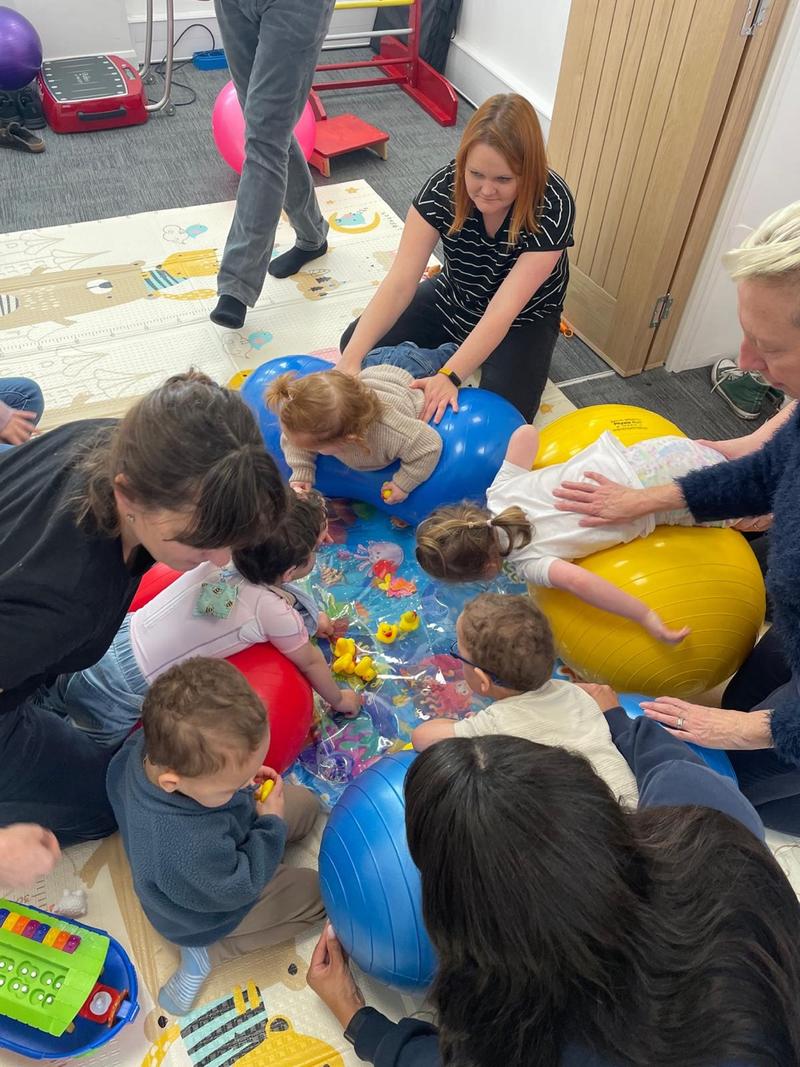 A physiotherapist supporting a smiling baby in sitting during a floor-based session