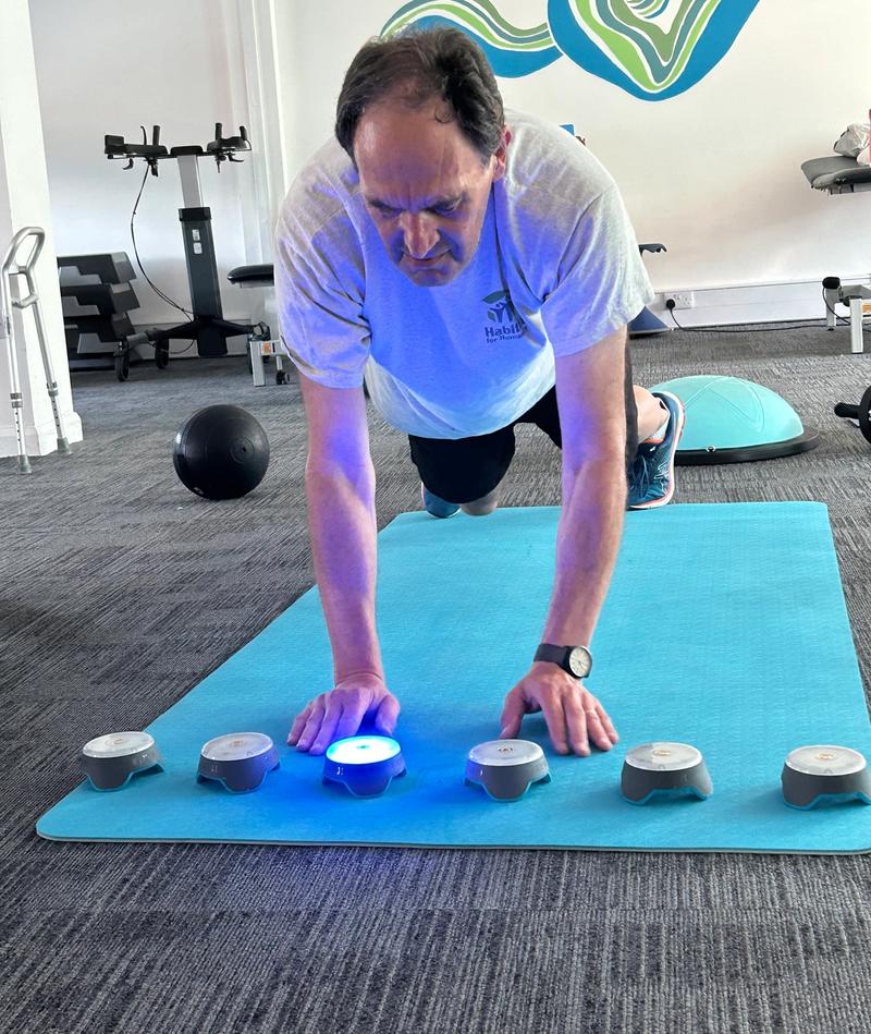 A client pressing a lit reaction pod while holding a press-up position