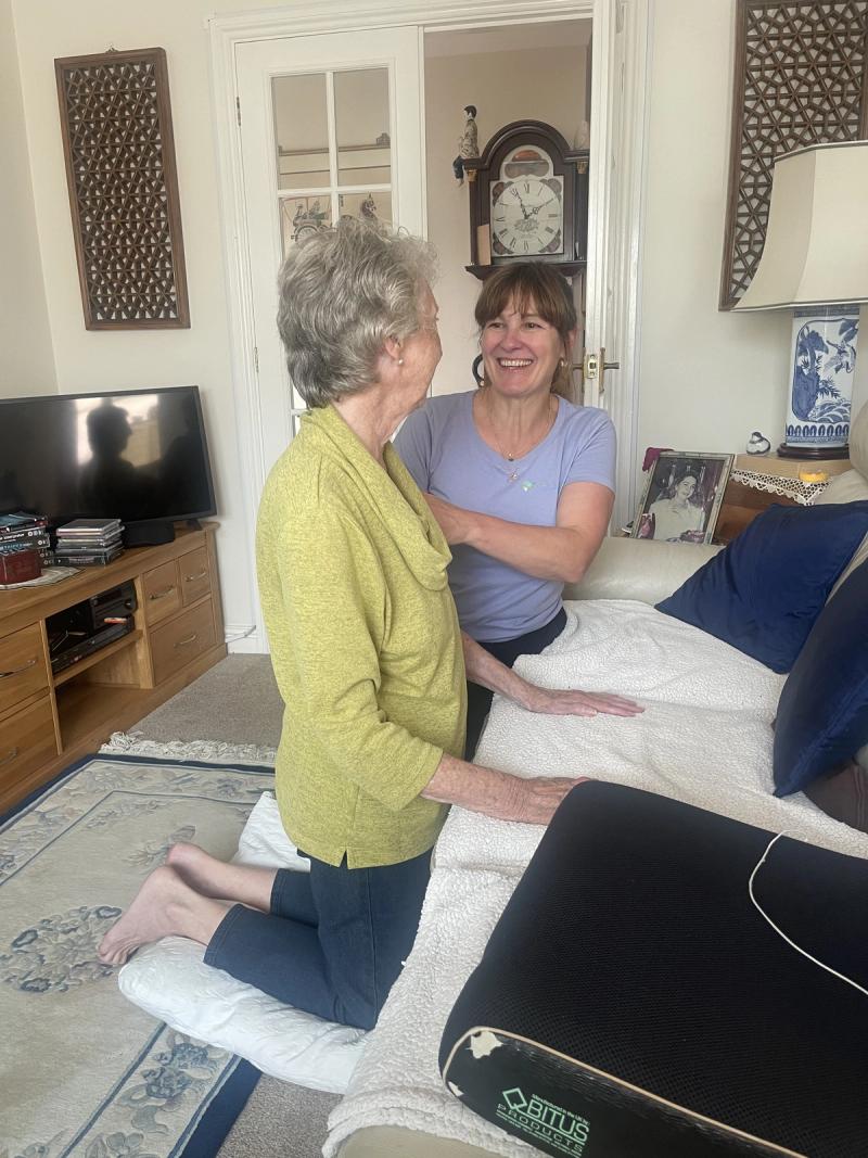 A physiotherapist supporting a client to kneel at the sofa during a home visit