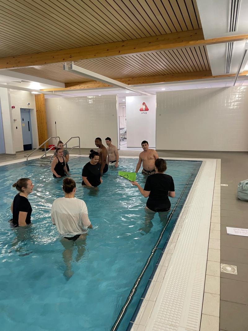 A hydrotherapy group in the pool while a therapist demonstrates an exercise