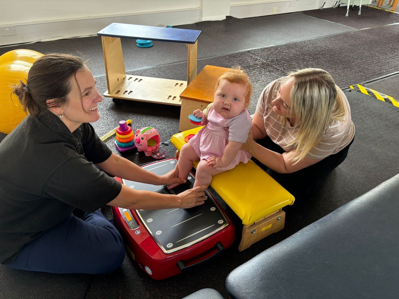 A physiotherapist and parent supporting a baby on the Galileo vibration plate during a play-based session