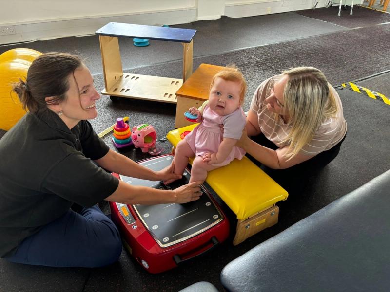 A physiotherapist and parent supporting a baby on the Galileo vibration plate during a play-based session