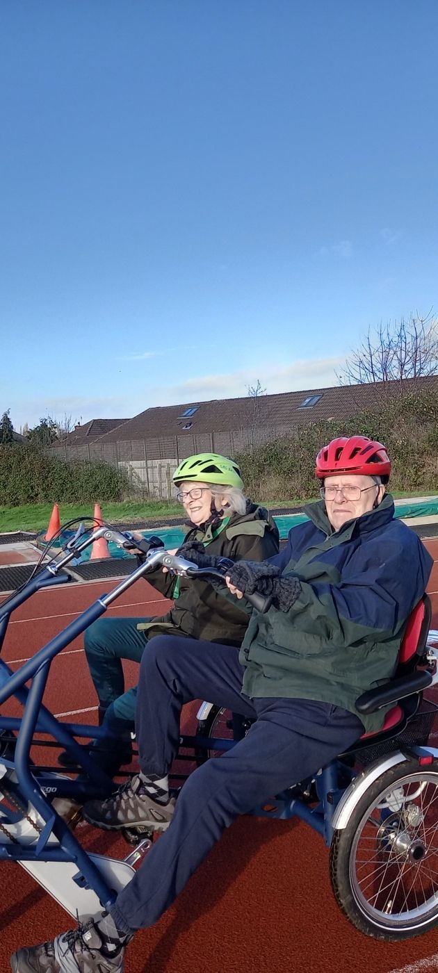 A client riding an adapted cycle outdoors during a community session