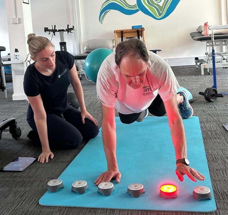 A physiotherapist watching as a client taps a lit reaction pod during a timed exercise
