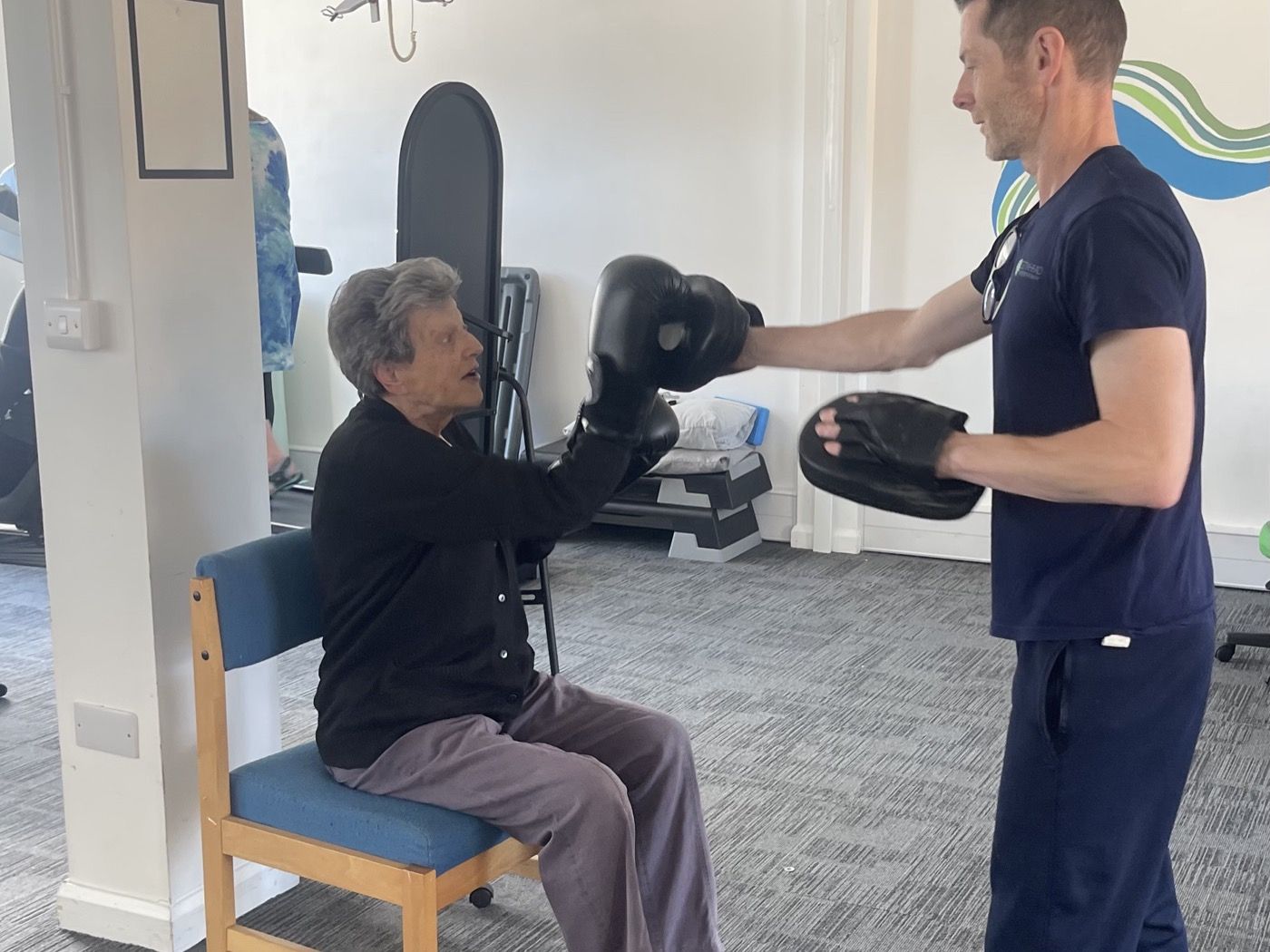 A physiotherapist holding boxing pads for a seated older client during a group exercise session