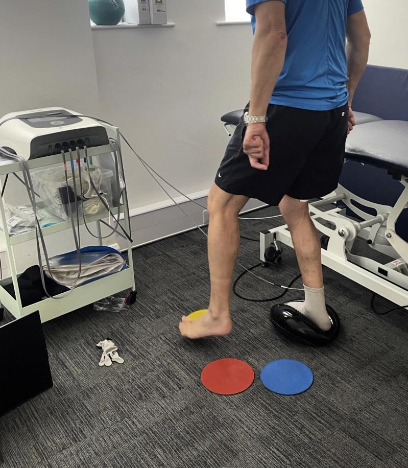 A client stepping between a balance cushion and a ball with stimulation electrodes attached