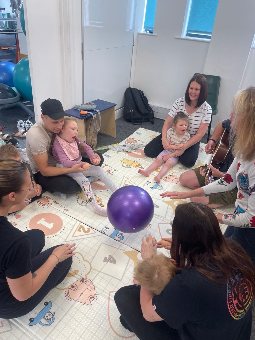 Parents, children and therapists sitting together with a gym ball during a Music and Movement group