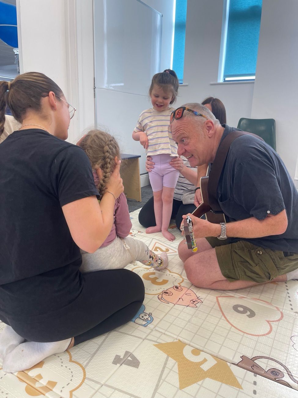 A music leader playing guitar for toddlers and parents during a Music and Movement session