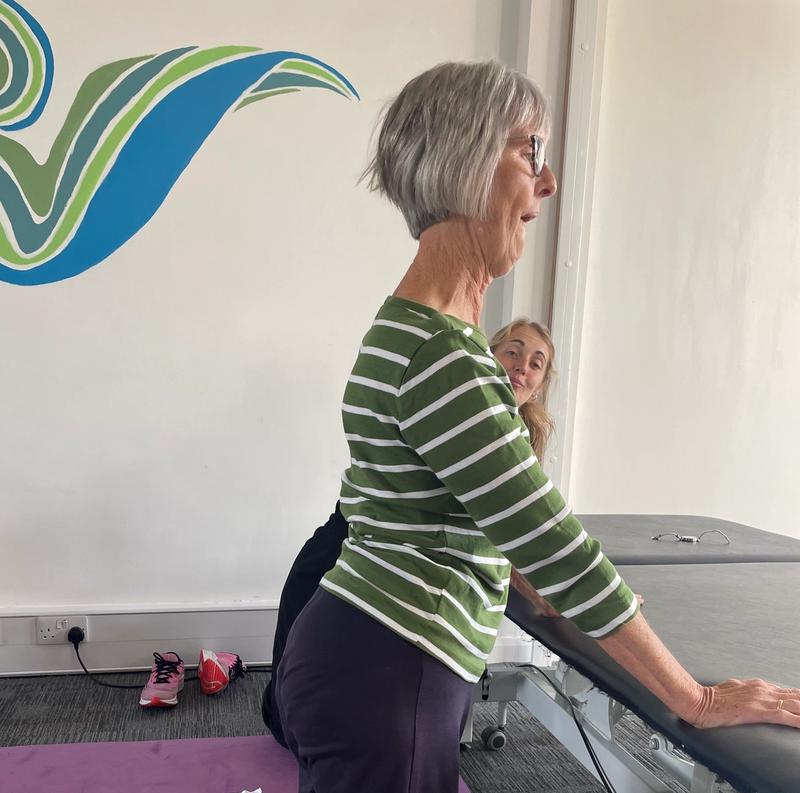 A client practising a kneeling position at the plinth with a physiotherapist supporting her