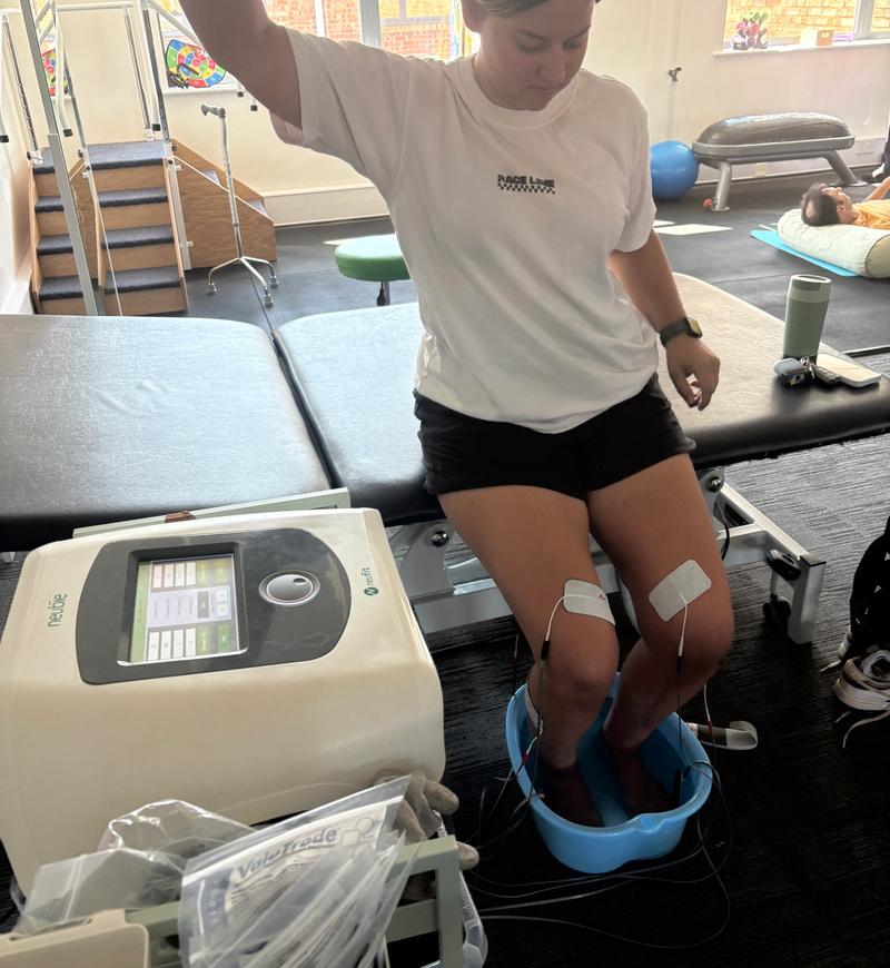 A client exercising with electrodes on both knees while the Neubie delivers stimulation