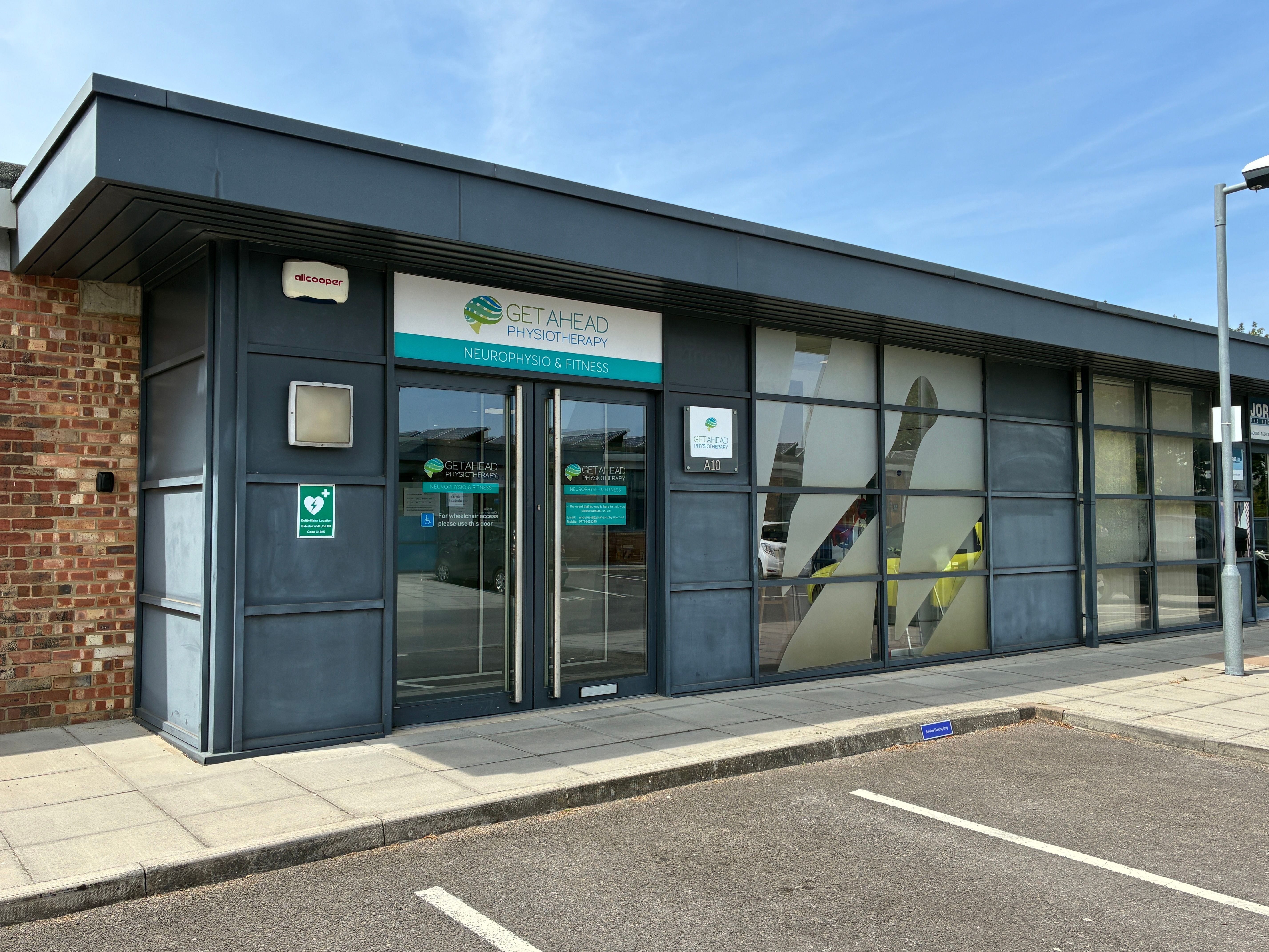 The entrance to the Get Ahead Physiotherapy clinic, with branded signage above glass doors, level access from the pavement and parking bays directly outside