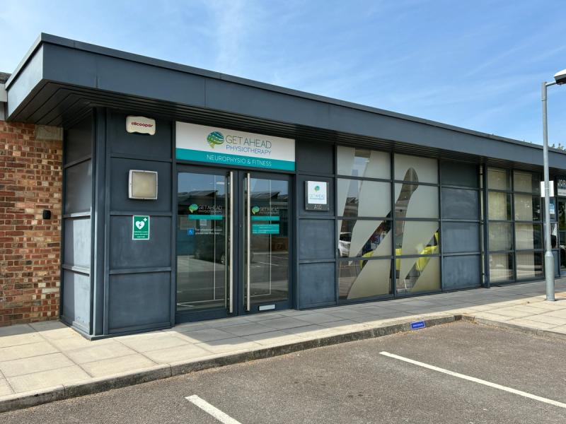 The entrance to the Get Ahead Physiotherapy clinic, with branded signage above glass doors, level access from the pavement and parking bays directly outside