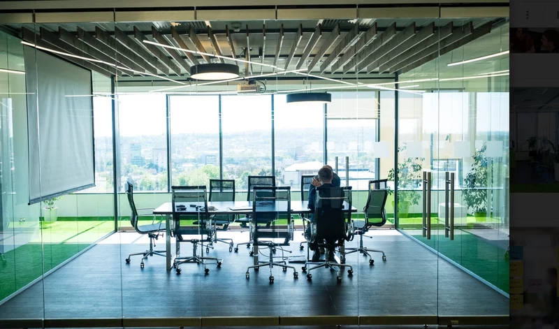 A colleague works in a large glass walled board room.