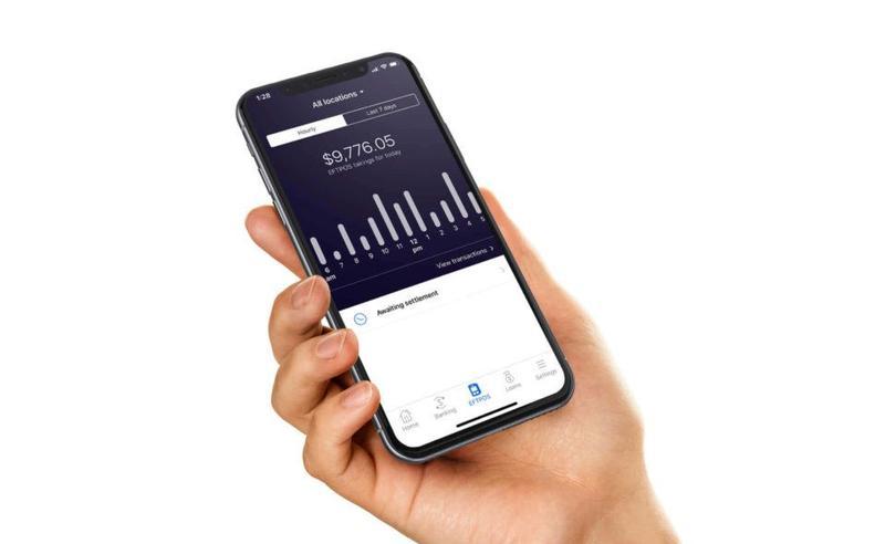 A hand holds a mobile phone showing a balance and a bar graph from the app