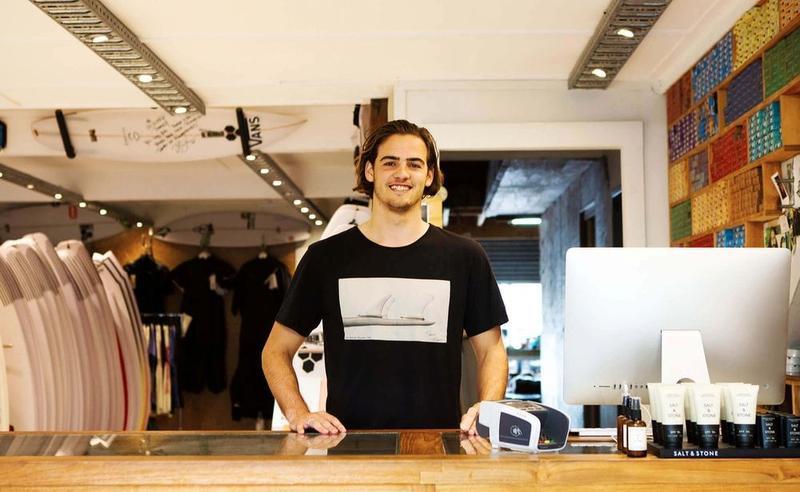 A man stands behind the counter in a surfing shop.