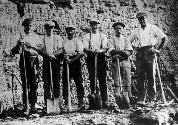 B&W photo of clay miners standing in row holding spades and pick axes