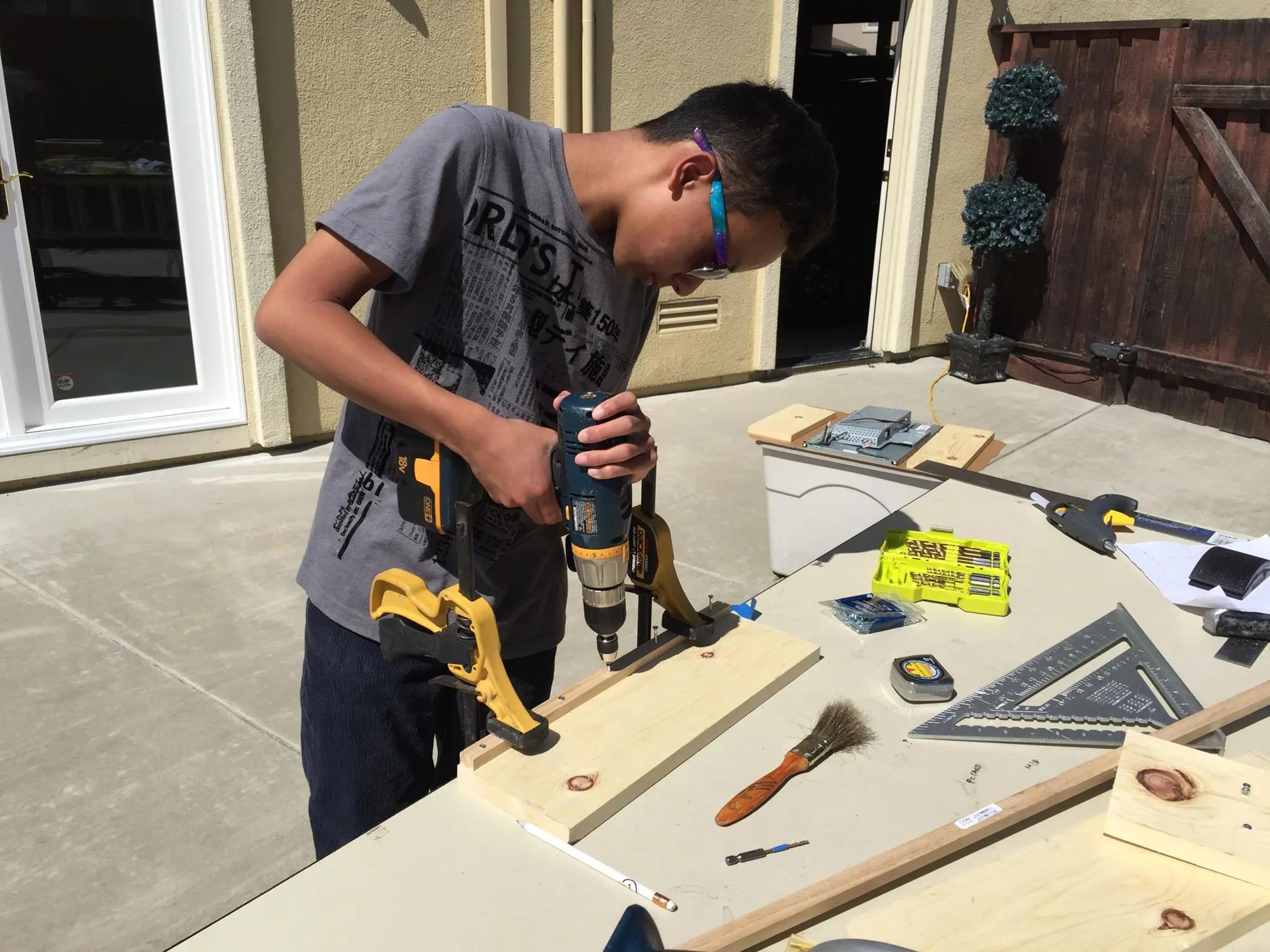 A picture of me drilling a thin piece of wood on a flat piece of wood.