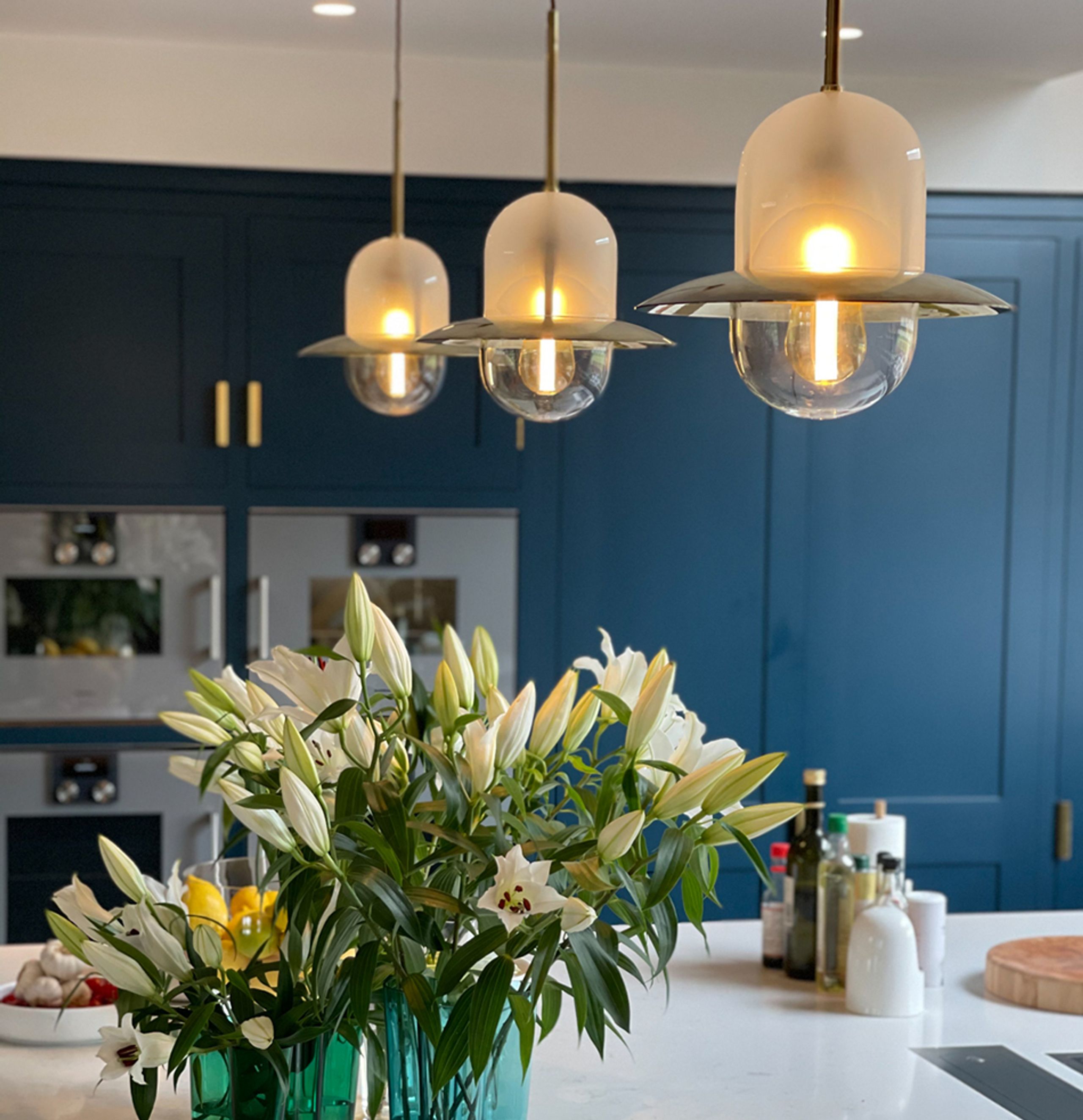 Pendant lighting in a completed residential kitchen Three illuminated glass pendant lights above a kitchen island with dark blue cabinetry