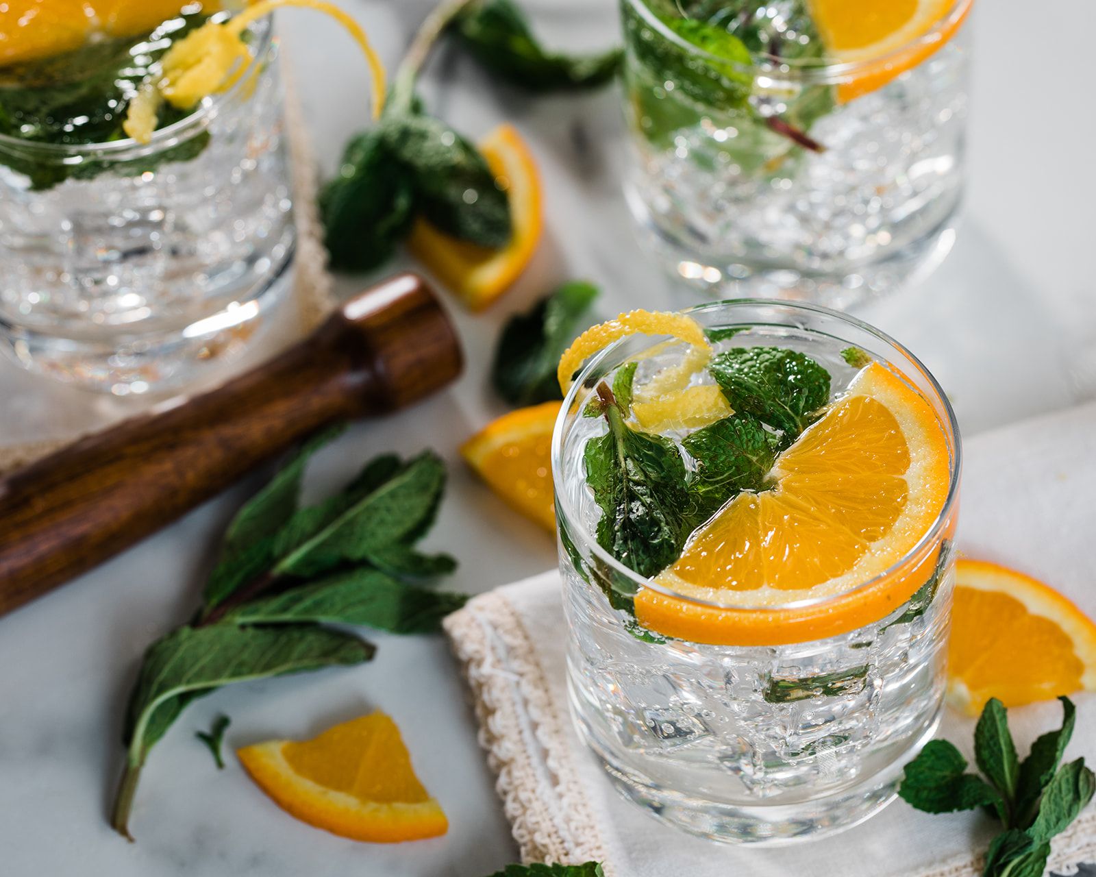 Clear alcoholic seltzer beverage with muddled mint and an orange slice.