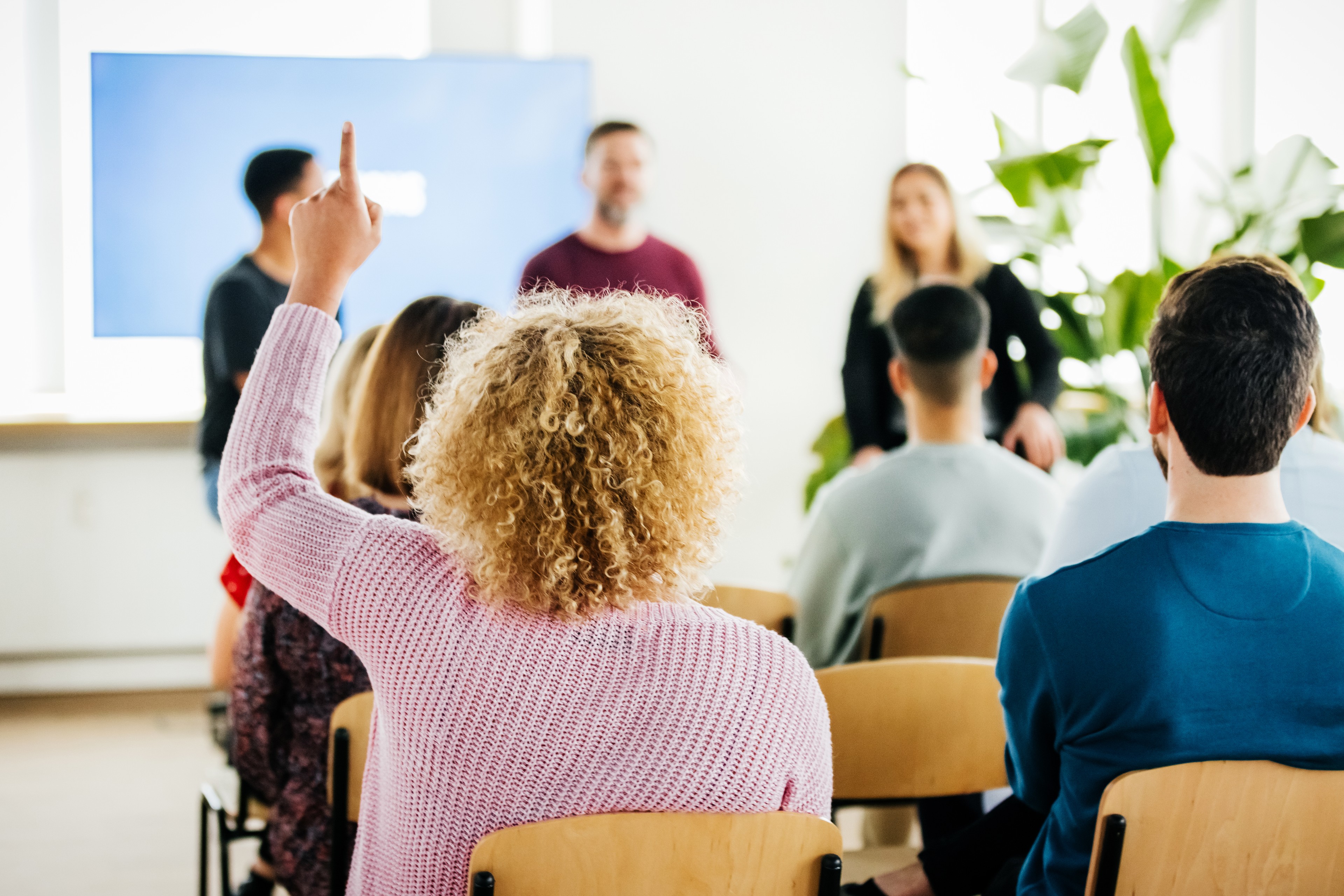 Woman Raising Hand To Ask Question During Presentation